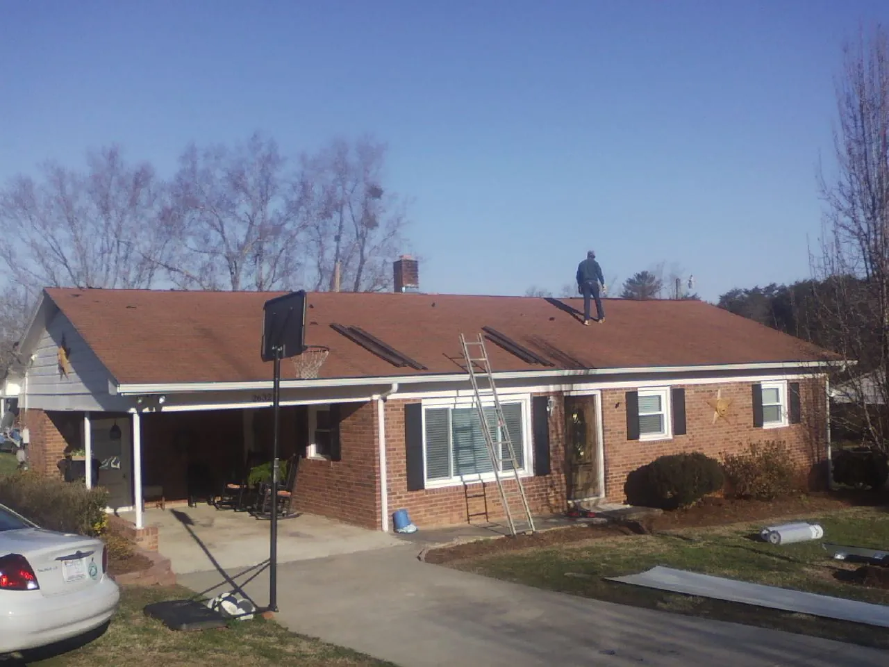 Roofer stripping a shingle roof on a brick ranch before metal panels in Moravian Falls