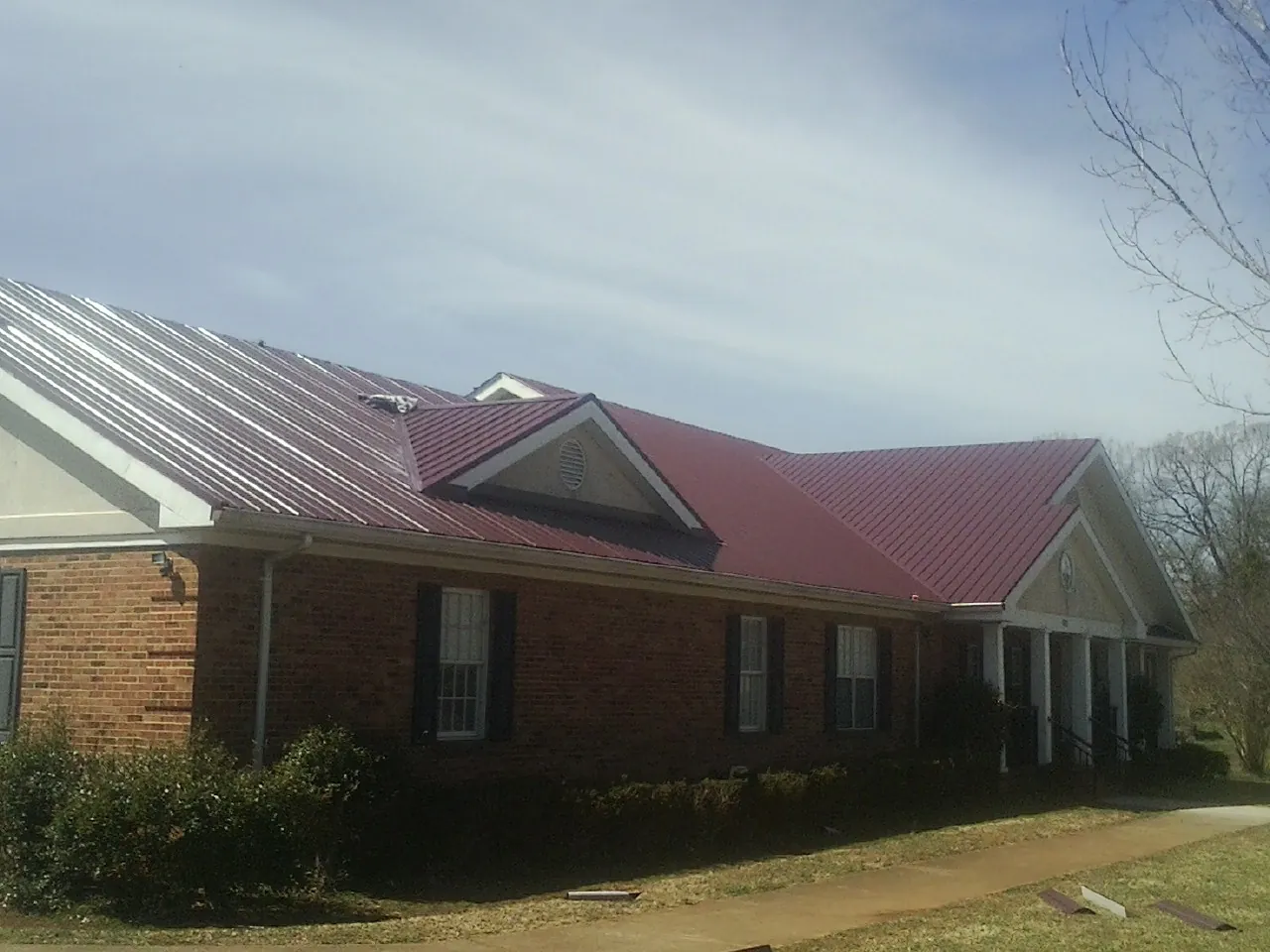 Red metal roof with gabled entries on a long brick building, from a Hail Damage Roof Repair job in Moravian Falls