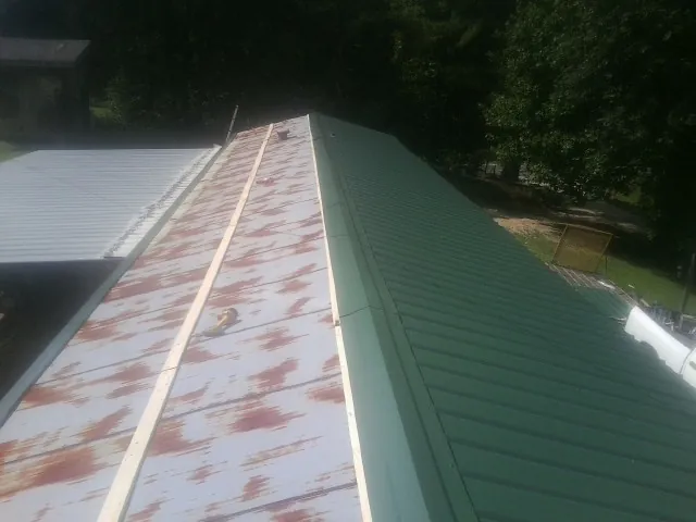 Old rusted panels beside newly installed green metal roofing — Wind Damage Roof Repair by Roofing Brothers in Moravian Falls