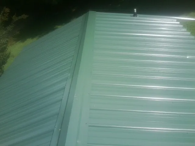 New green metal panels meeting at the ridge of a roof — Flat Roof Repair work by our crew in Moravian Falls