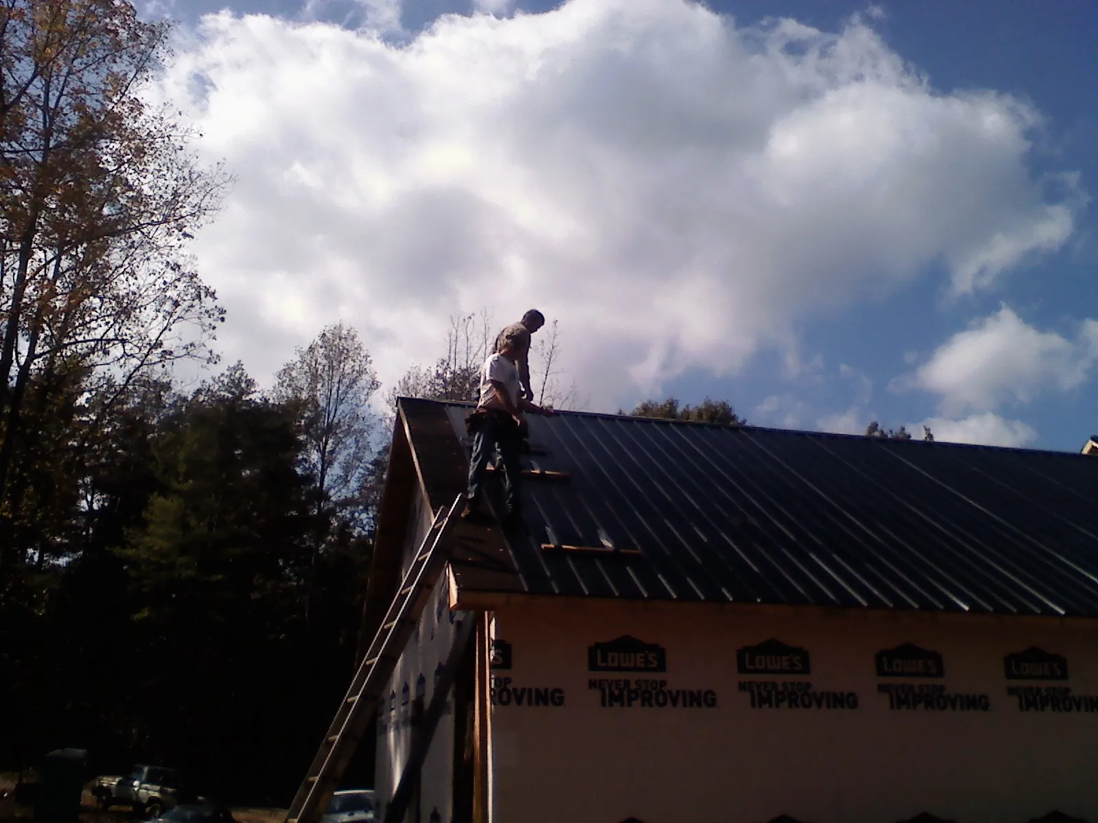 Roofer fastening dark metal panels high against a cloudy sky, from a Roof Inspection job in Moravian Falls
