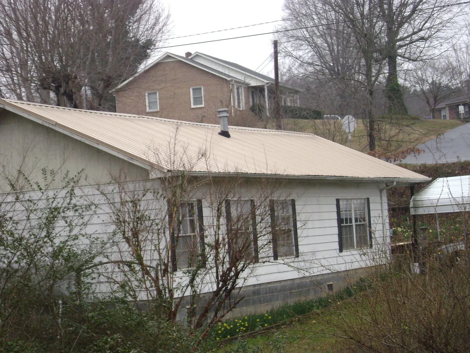 Tan metal roof on a white sided house set into a hillside — Commercial Roofing by Roofing Brothers in Moravian Falls