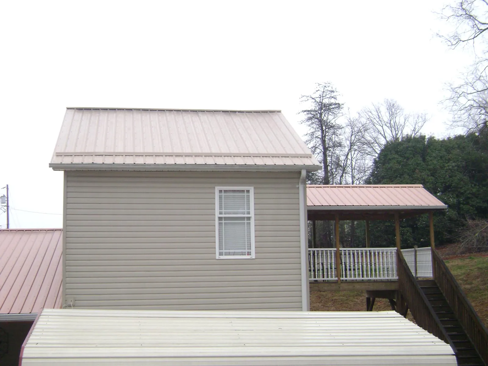 Tan metal roofs on a two story addition and attached porch, from a Roof Replacement job in Moravian Falls