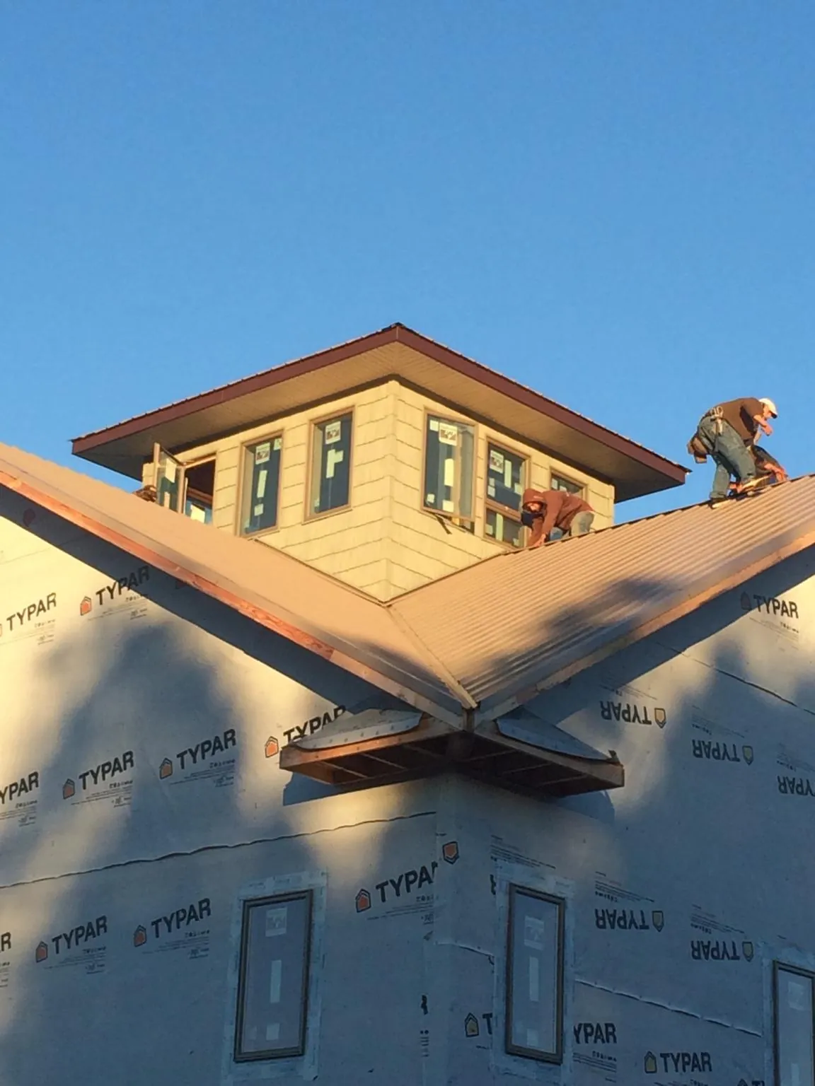 Roofers working around a rooftop cupola on a new metal roof at sunset — Roof Waterproofing in Moravian Falls by Roofing Brothers